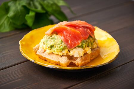 Belgian waffle with scrambled egg, avocado and salmon on wood table. Plate, bacon. Keto Breakfast variationの写真素材