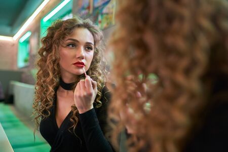 Portrait of curly young woman applying lipstick.の写真素材
