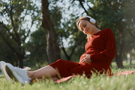 Pregnant woman listening to a music at park.