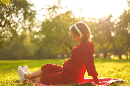 Pregnant woman listening to a music at park.の写真素材