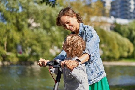 Happy woman riding on an e-scooter with her son. Young and beautiful caucasian woman rides electric...