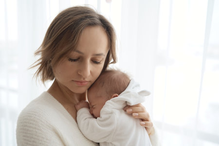 Beautiful woman breastfeeding her baby in a cozy house on the bed.の写真素材