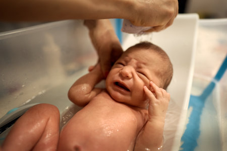 Small baby first bathing on mother hands, bathing in small plastic bathの写真素材