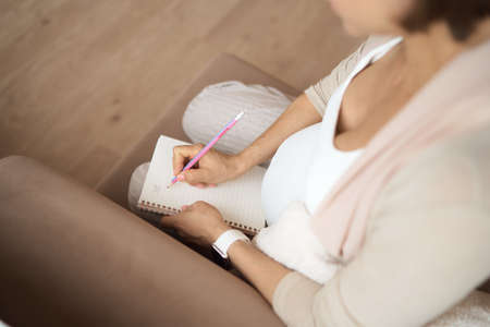 Pregnant woman makes notes. Concept of pregnancy, health care, medicine. Mother waiting of baby at the home.の写真素材