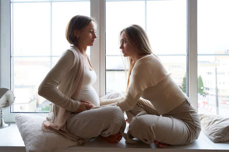 Smiling woman touching belly of pregnant girlfriendの写真素材