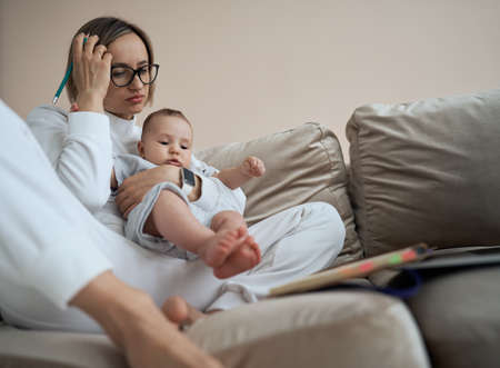 Young mother working on a laptop. Business Woman working from home with little girl. Work on maternity leave.の写真素材