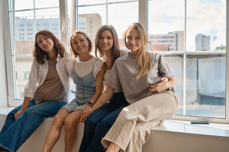 Girls having fun on window sill. Four caucasian girls sitting on window sill discuss something and lough. Art school workshop.の写真素材