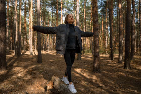 A girl walks on a log in a pine forest in autumn. Girl balancing on a log in the forestの写真素材