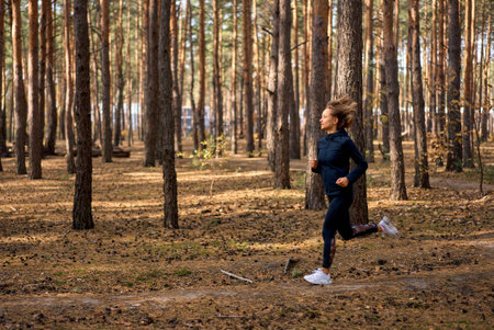 Young athletic woman jogging in forest in sunny morning. Healthy lifestyle concept