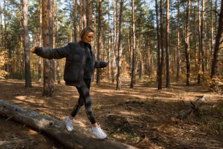 A girl walks on a log in a pine forest in autumn. Girl balancing on a log in the forestの写真素材