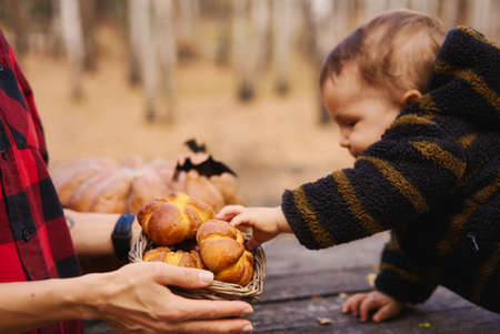 Young woman and her baby son in autumn park, boy playing with helloween pumpkin and eating pumpkin bun.の写真素材
