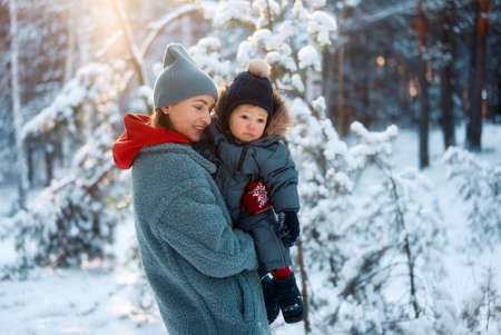 Young mother and her baby playing in the snowy forest. Young mother carrying her baby in the forest on a very snowy dayの写真素材