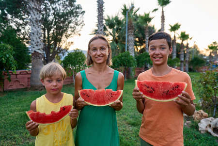 Sweet family, mother and her kids eating watermelon outdoor and having funの写真素材