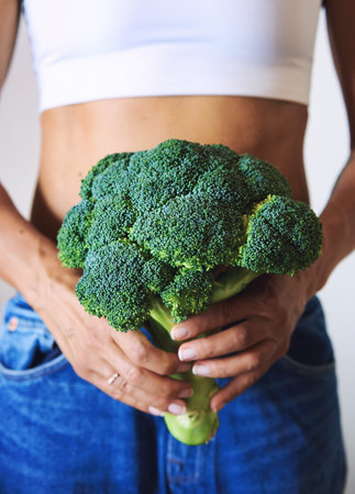 young woman dressed in white t-shirt showing with broccoliの写真素材