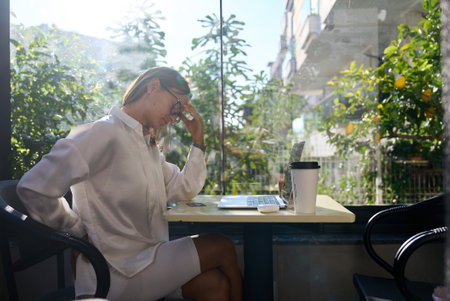 Tired stressed woman suffering from neckpain working from home office sitting at table. Overworked young aged lady massaging neck feeling hurt pain from incorrect postureの写真素材