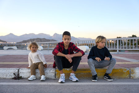 Three brothers sitting outside on a sidewalk and have fun.の写真素材