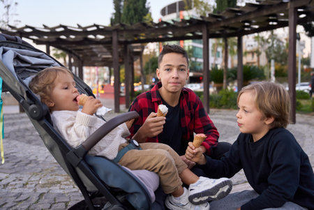 Three brothers boys with ice cream in city park.の写真素材