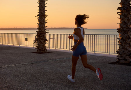 Woman running jogging at sunrise sunset silhouetted with palm trees and ocean in backgroundの写真素材