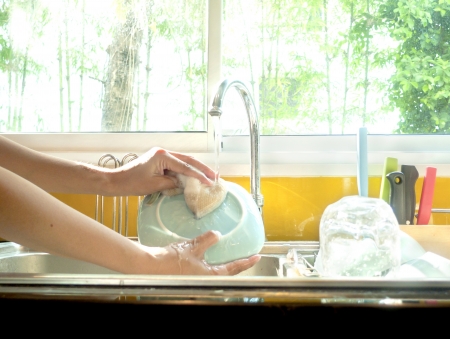 Hands washing dishes with running water from faucet in sinkの写真素材