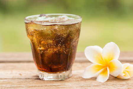 glass of cola with ice cubes on wood