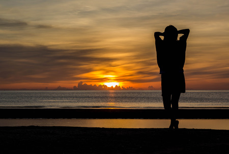 Young woman standing on the beach in sea and looking to sunrise.の写真素材