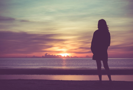 Young woman standing on the beach in sea and looking to sunrise.の写真素材