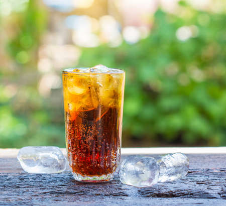 glass of cola with ice cubes on wood table.の写真素材