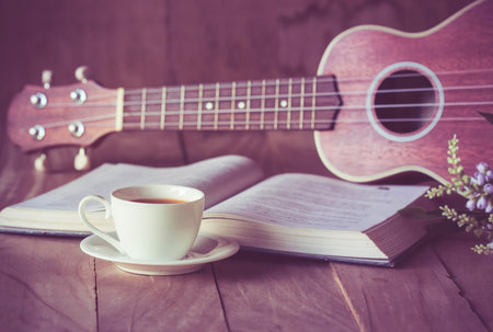 Cup of tea on table with ukulele and book.の写真素材