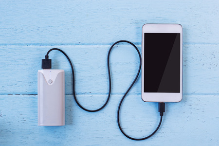 Smartphone charging with power bank on wooden table.の写真素材