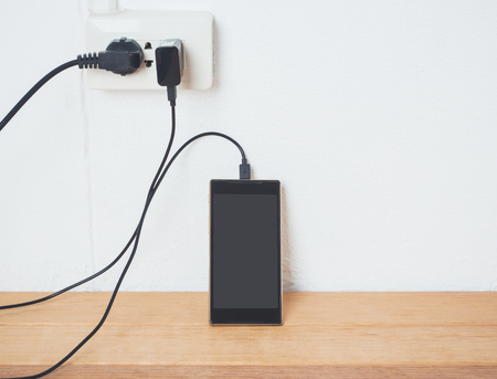 Mobile phone in charging plugged on white wall,low battery and charge concept.の写真素材