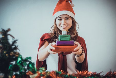 Cute woman holding a Christmas gift over gray background.の写真素材