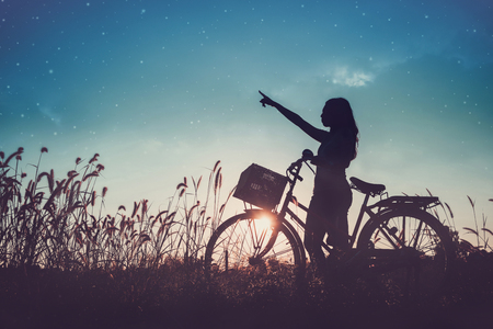 Women relaxing with a bike in the meadow at sunset.の写真素材