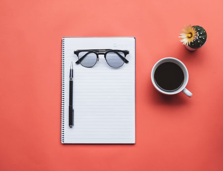 Top view image of notebook with cup of coffee and glasses on orange background.