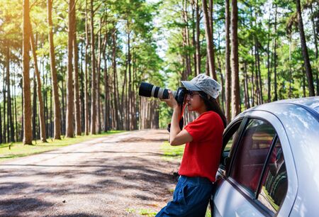 Young asian woman travels by car take a photograph in pine forest.の写真素材
