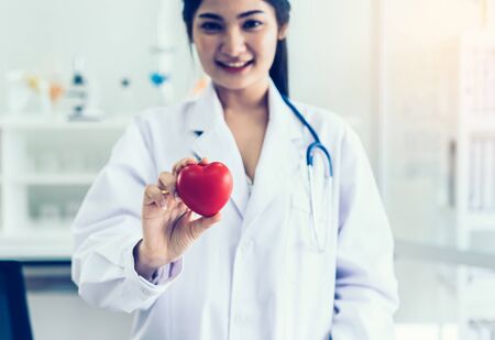 Female doctor with stethoscope holding a red heart, Healthcare and cardiology concept.の写真素材