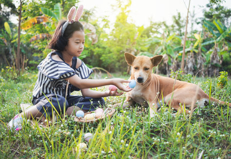 Cute little gril wearing bunny ears and basket with eggs and dog on green grass.の写真素材