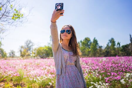Beautiful happy asian woman taking a selfie in cosmos flower field.の写真素材