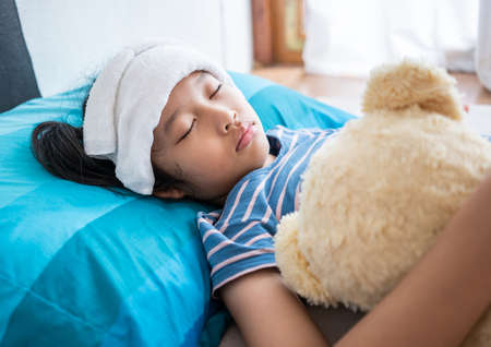 Sick little girl sleep with Teddy Bear in bed room at home,Compress on forehead.の写真素材