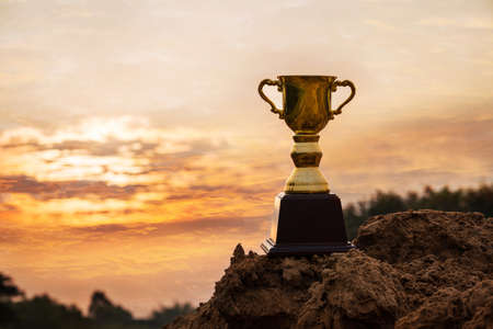 Win concept,Gold trophy cup on top mountain with sunrise sky background.の写真素材