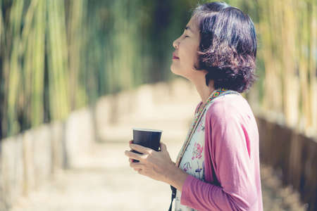 Side view portrait of a asian woman with coffee relaxing breathing fresh air relaxing in park.の写真素材