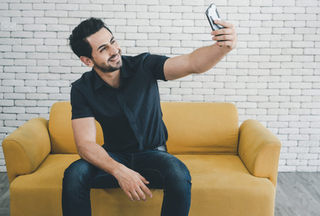 Portrait of a smiling man making selfie photo and sitting on sofa.