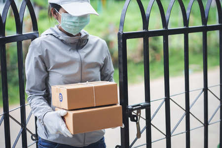Delivery woman holding shopping box and medical rubber gloves and mask delivering packages at door. Online shopping and Express delivery.の写真素材