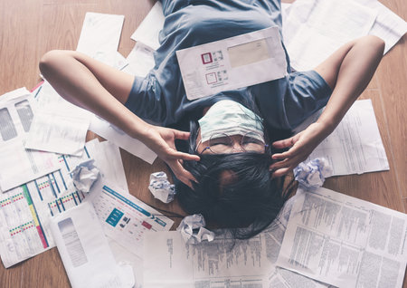 Top view of stressed young asian woman hands holding the head worry about the debts and bills.の写真素材