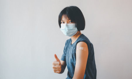 Asian girl wearing protective mask against covid-19 with showing her arm after getting vaccine.の写真素材