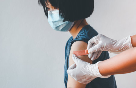 Asian girl wearing protective mask against covid-19 with showing her arm getting plaster after got vaccine.の写真素材
