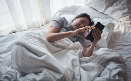 Woman  lying in bed using and looks at a smartphone. Internet and cell phone addiction.Insomnia, phobia, Dependency on a cell phone.の写真素材