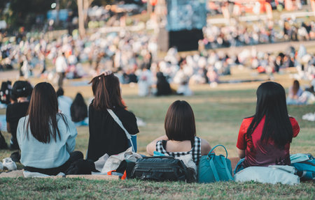 Back view of female friends watching concert in the park at open air, sitting in front of stage.の写真素材
