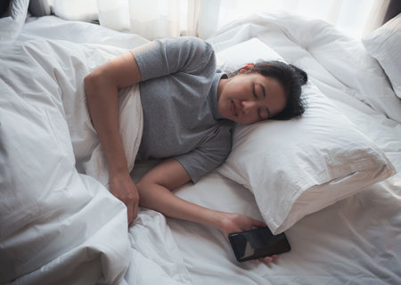Woman sleeping fell asleep in bed with white screen smartphone. Internet and cell phone addiction.の写真素材