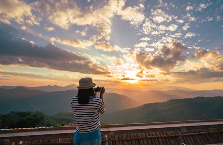Back view of young woman using camera for making picture of sunset ver the mountain.の写真素材