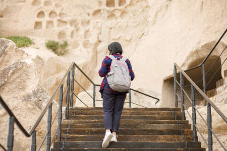 A girl traveler with a backpack on her back climbs the steps up a mountain hill, historical valueの写真素材
